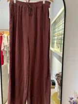 Pantalón ancho de lino color marrón oscuro (chocolate), con cintura elástica fruncida y lazo ajustable. Presenta bolsillos laterales.