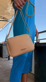 Bandolera pequeña de símil cuero color gris con textura granulada. Posee dos compartimientos principales con cierre y un bolsillo frontal con cremallera metálica. Incluye correa fina ajustable y extraíble.