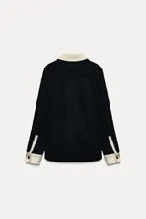 Camisa negra de terciopelo con cuello solapa, manga larga con puños en tejido color crema a contraste y bajo redondeado.