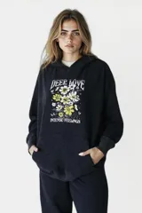 Buzo negro con capucha y cordones ajustables, mangas largas con puños ajustados y estampado frontal de flores amarillas y blancas con texto en blanco.