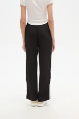 Pantalón de algodón negro, holgado, de calce medio, con cintura elástica y cordón ajustable. Presenta tres rayas blancas verticales en los laterales.