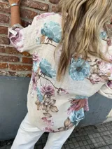 Camisa beige con estampado de flores rosas y celestes, cuello mao, cartera con tres botones y mangas 3/4 con botón para sujetar.