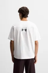 Camiseta blanca de corte holgado, cuello redondo y manga corta. Estampado frontal con texto en color negro y parche en la espalda. Detalle de pliegues en la espalda.
