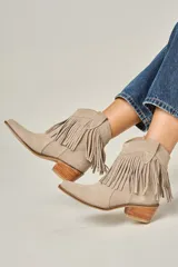 Bota tejana de cuero color beige, con flecos en la caña, taco de madera y punta fina.