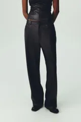 Pantalón marrón de tiro medio con trabillas en la cintura, cinco bolsillos y pernera ancha. Cierre frontal con cremallera, botón oculto y gancho metálico.