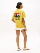 Remera amarilla de algodón con corte amplio, cuello redondo y hombros caídos. Presenta un logo pequeño de Tommy Hilfiger en el pecho, un logo en la manga y un logo grande en la espalda. Pertenece a la colección Hilfiger Sailing.