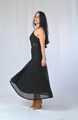 Vestido largo negro con escote halter, espalda descubierta, corte a la cintura con transparencias laterales y falda amplia con bordado calado en el ruedo.