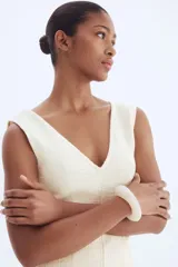 Vestido corto sin mangas color blanco roto, con escote en V pronunciado y textura de tejido bouclé. Presenta costuras moldeadoras en el frente y la espalda, y un bajo con flecos.