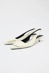 Zapato destalonado color crema con tacón fino y adorno en la parte delantera.