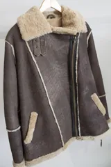 Campera gamulán marrón con interior de piel sintética color beige, cierre cruzado con cremallera y cuello con solapas amplias.