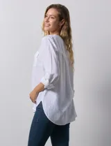 Blusa blanca de lino y rayón, con cuello a la base, escote en V y abertura con botones. Tiene bolsillos en la parte delantera y mangas largas regulables con presilla y botón.