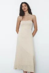 Vestido midi de encaje color crudo, con escote recto y hombros descubiertos. Detalle de tira con lazo combinada a tono. Forro interior y cierre lateral con cremallera oculta en costura.