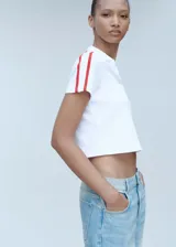 Polo blanco de corte entallado, con cuello clásico, mangas cortas y dos rayas rojas en los hombros.
