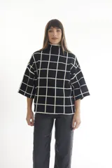 Sweater color crema con cuello alto y mangas cortas anchas, con diseño de cuadros negros.