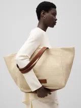 Bolso tipo shopper grande color beige, con textura tipo rafia y asas de cuero marrón.