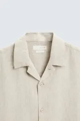 Camisa color marrón oscuro de corte relaxed fit, confeccionada en tejido de lino. Tiene cuello bowling, manga corta, bajo con aberturas laterales y cierre frontal de botonadura.
