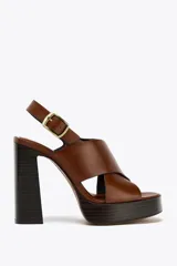 Sandalias de cuero color marrón con plataforma y tacón cuadrado de madera. Tiras anchas cruzadas en el empeine y tira trasera con hebilla dorada.