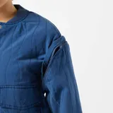 Chaqueta azul acolchada con cuello redondo, cierre con botones a presión, mangas largas con puños elásticos, dos bolsillos frontales con solapa y hombreras.