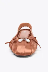 Zapato plano destalonado color marrón, con efecto satinado, detalle de fruncidos en la punta, lazo con perla en la parte delantera, tira elástica en el empeine y acabado en punta redonda.