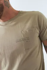 Remera color arena de algodón, corte regular, manga corta, cuello redondo y bolsillo en el pecho con estampado de texto.