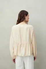 Blusa color beige de caída fluida con cuello redondo y lazos frontales. Diseño con cortes horizontales y frunces, mangas largas con puños elastizados.