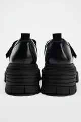 Zapato tipo mocasín negro con plataforma y suela track. Presenta tira ajustable adherente y tirador trasero.