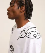 Remera blanca de corte oversized, confeccionada en tejido de malla de algodón. Presenta cuello redondo, mangas cortas y estampados con lettering y motivos maoríes en color negro.