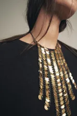 Collar tipo babero con flecos de piezas metálicas doradas y cadena de eslabones negros.