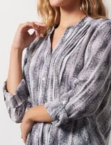 Blusa de gasa estampada con cuello a la base, escote en V y abertura central con botones. Delantera con plisados y mangas 3/4 regulables con presilla y botón.