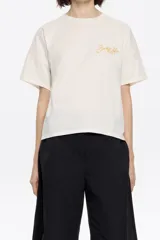 Camiseta color crudo de algodón, con cuello redondo y mangas cortas. Presenta logo bordado en color dorado en el frente.