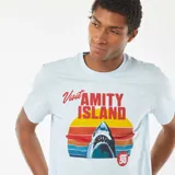 Camiseta celeste con estampado de la película Jaws (Tiburón) con el texto "Visit Amity Island" y el logo del 50 aniversario. 