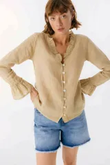 Blusa blanca de lino con botones de nácar, volados en el escote y mangas largas con puños acampanados. Corte recto y holgado.