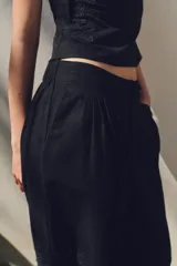 Pantalón negro con bordados florales en los laterales, tiro alto, cintura elástica en la parte trasera, bolsillos laterales, pliegues y cierre frontal con cremallera, botón interior y gancho metálico.