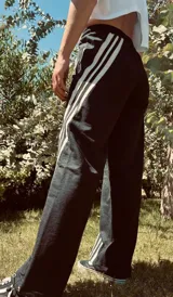 Pantalón deportivo negro de corte ancho con tres rayas blancas verticales en los laterales.