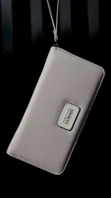 Billetera larga negra con cierre perimetral y placa metálica con logo. Posee múltiples compartimentos internos para tarjetas y documentos, además de un bolsillo con cierre interior. Incluye correa de mano desmontable.