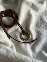 Collar con cordón fino de gamuza marrón y dije de aro de bronce.
