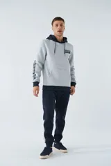 Buzo canguro gris con capucha ajustable y bolsillo delantero. Tiene puños y cintura acanalados en azul marino, y un parche con texto en el pecho.