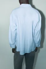 Camisa amplia color negro confeccionada con hilatura de lino. Tiene cuello solapa, manga larga, bolsillo de plastrón en el delantero, bajo asimétrico y cierre frontal con botones.