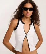 Musculosa blanca sin mangas, con cuello redondo y cierre frontal con cremallera. Presenta detalles contrastantes en negro en cuello y sisas. Diseño seamless.