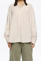 Camisa de corte recto en color beige claro, confeccionada en tejido fantasía con minibrillantes distribuidos por toda la prenda. Presenta cuello camisero y mangas largas con puño abotonado.