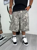 Pantalón ancho tipo baggy de tela estampada con patrón de camuflaje abstracto en tonos grises y beige. El largo es a media pierna, estilo bermuda ancha, con puños doblados.