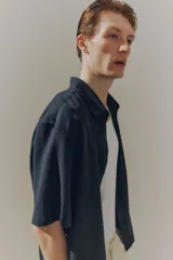 Camisa negra de manga corta en mezcla de lino y viscosa, con cuello inglés, tapeta lisa, canesú en la espalda y bajo recto. Corte holgado.