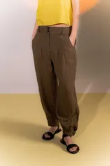 Pantalón de lino color marrón, con corte tipo barrel, tiro medio, pretina ancha con doble abotonadura, bolsillos laterales y pinzas en el frente. Ruedo con presilla permitiendo usarlo recto o fruncido al tobillo.