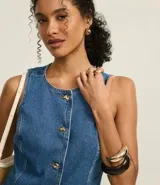 Chaleco femenino confeccionado en jeans, sin mangas, cinturado, con botones y bolsillos. De corte alargado y cuello redondo.