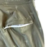 Short de baño verde militar con estampado de palmeras, pretina fija con hebillas metálicas laterales, botón a presión, cierre frontal, tres bolsillos (dos laterales y uno trasero), tela con spandex de secado rápido e interior de mesh hipoalergénico.