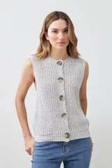 Chaleco tejido gris con botones de madera, sin mangas y cuello redondo.