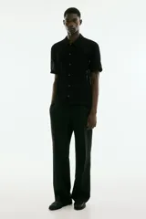 Camisa negra de manga corta con tejido calado tipo crochet, cuello inglés, botones frontales y corte recto.