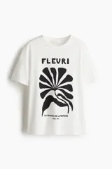 Remera de manga corta y cuello redondo, color blanco, con estampado frontal en negro que incluye la palabra "FLEURI", una ilustración abstracta de una hoja o flor y el texto "LA BEAUTÉ DE LA NATURE PARIS, 1978".