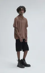 Camisa de tejido de punto color café, manga corta y cuello polo con botones frontales. Presenta un patrón calado de espiga o chevron.