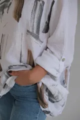 Blusa blanca de lino con estampado abstracto en tonos marrones y grises, de corte holgado y mangas 3/4 con puños abotonados.
